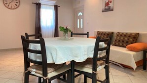 Un comedor con una mesa redonda, sillas, un jarrón con flores, un reloj y un sofá con cojines.