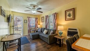 A cozy living room with a sectional sofa, a dining table, and a ceiling fan. - Quaint Cabin By The Creek Privat (Pipestem)