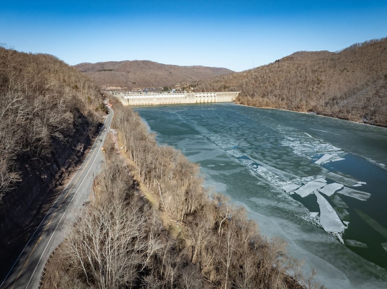 Un barrage avec une route qui longe une rivière, le tout étant entouré de collines.