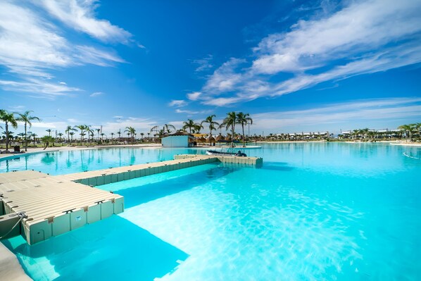 A large outdoor swimming pool with clear blue water, surrounded by palm trees and a clear sky.