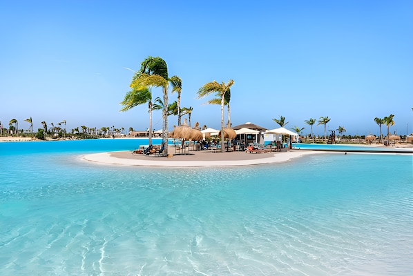 A tropical beach resort with clear blue waters, palm trees, and a central building with a pool.