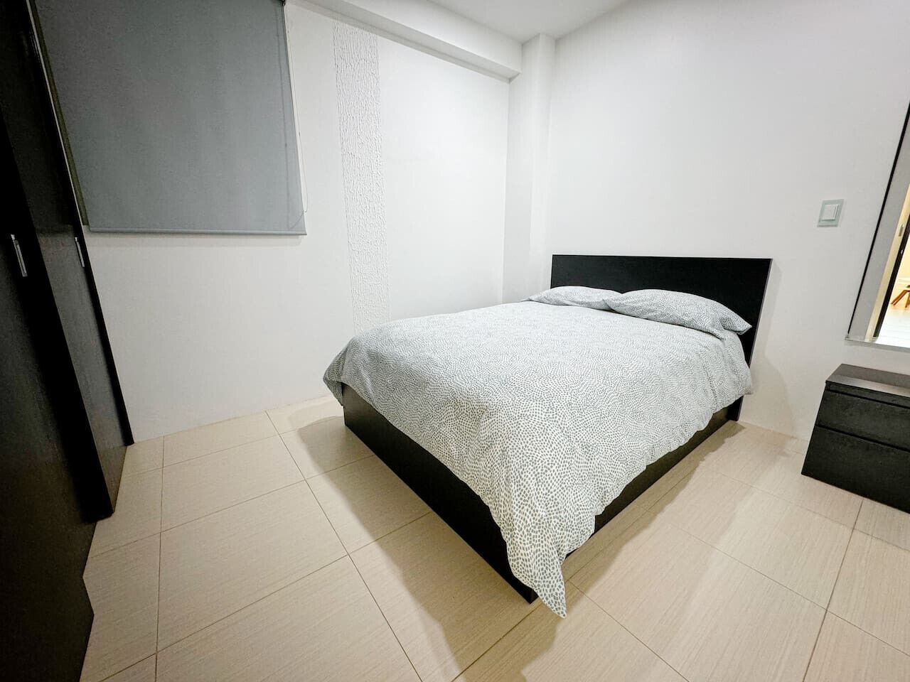 A bedroom with a bed, a nightstand, a wardrobe, and a window with curtains.