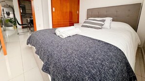 Una cama bien hecha con una manta gris y blanca, un cabecero gris y un cojín estampado con rayas.