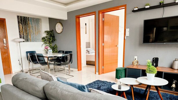 Una sala de estar moderna con un sofá gris, un comedor con una mesa y sillas, y un televisor montado en la pared.