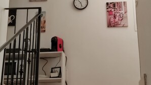 Eine Treppe mit einer Wanduhr, einem Regal mit einem rosafarbenen Gegenstand und Wanddekoration, darunter ein Fahrrad und ein Motiv mit Kaffee.