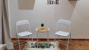 Ein Zimmer mit zwei weißen Stühlen, einem kleinen Tisch mit einer Pflanze und einem an der Wand befestigten Regal mit Dekoration.