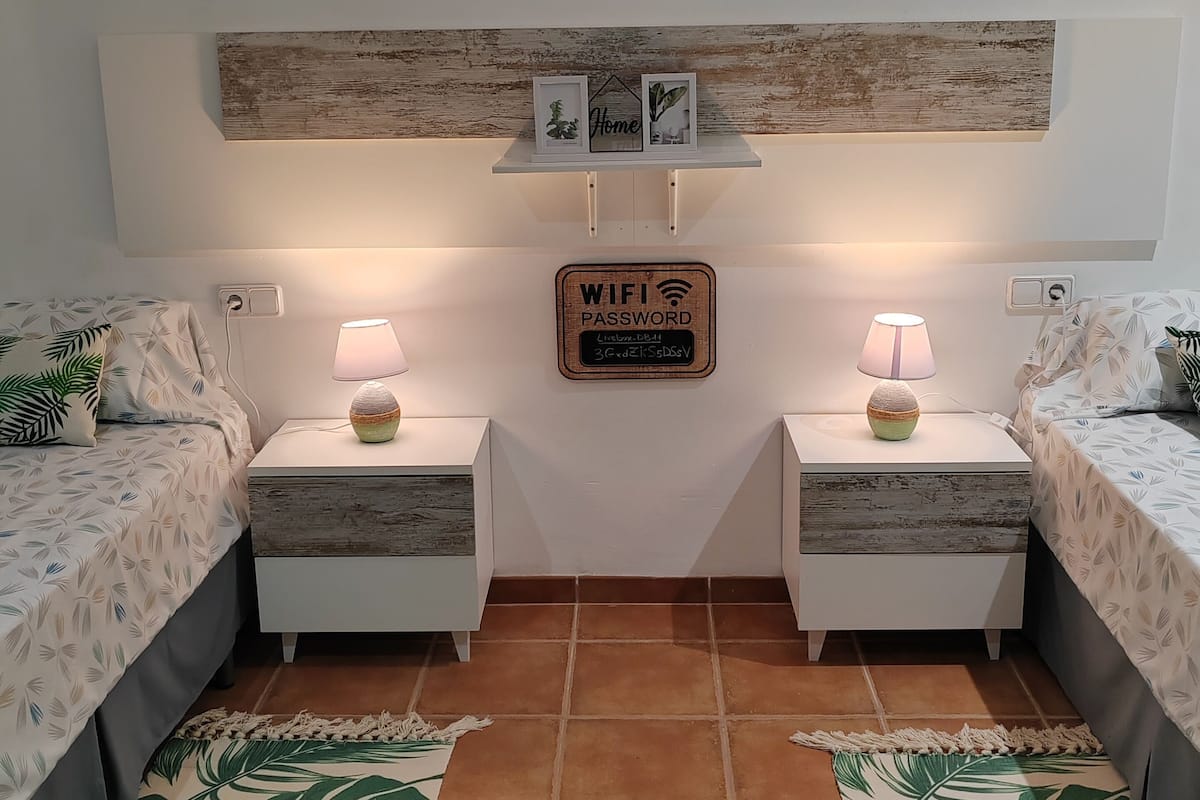 A bedroom with two beds, a wooden headboard, a painting, a signboard, and a patterned rug.
