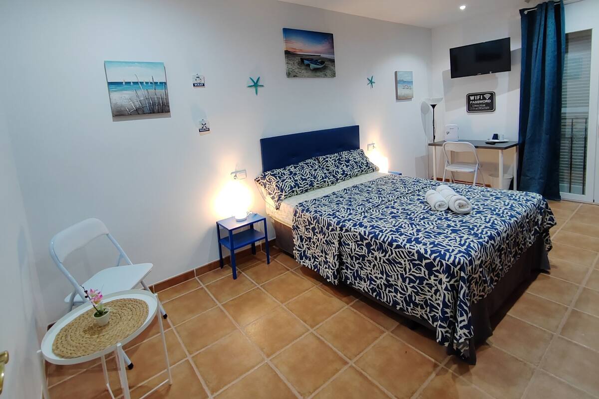 A bedroom with a bed, a desk, a chair, and a small table with a plant.
