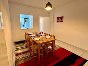 A dining area with a wooden table set for six, a red patterned rug, and a pendant light above.
