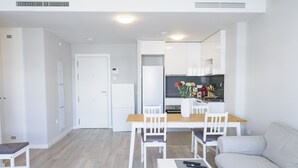 Ein modernes Wohnzimmer mit einer Couch, einem Esstisch mit Stühlen, einem Fernseher und einem Kühlschrank.