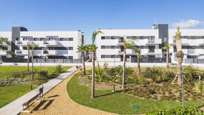 Ein modernes Gebäude mit mehreren Balkonen und einem angelegten Garten mit Palmen.