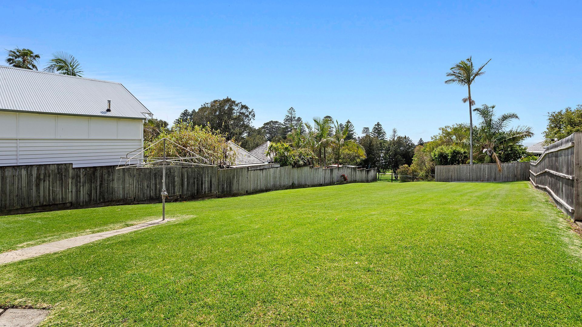 A backyard with a well-maintained lawn, a wooden fence, and a house in the background.