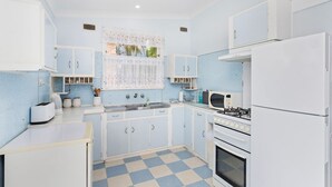 A compact kitchen with white cabinets, a checkered floor, a gas stove, a microwave, and a refrigerator. - Jack's Place - Cozy Retreat (Gerringong)