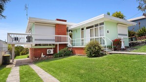 A two-story house with a balcony, a brick chimney, and a small garden with a lawn and a pathway. - Jack's Place - Cozy Retreat (Gerringong)