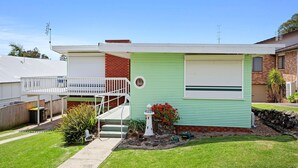 A single-story house with a front porch, a small garden with red flowers, and a garage. - Jack's Place - Cozy Retreat (Gerringong)