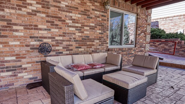 A covered patio with a wicker sectional sofa and a small table.