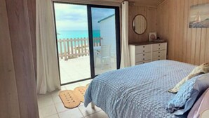 Une chambre avec un grand lit, une commode et une vue sur la plage, accessible par une porte coulissante.