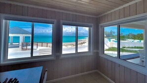 A room with large windows offering a view of the ocean and a resort area. - Sea La Vie - Schooner's Landing (Man-O-War Cay)
