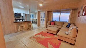 A spacious living area with a large sofa and a red rug, a kitchen with modern appliances, and a view of the sea through large windows. - Sea La Vie - Schooner's Landing (Man-O-War Cay)