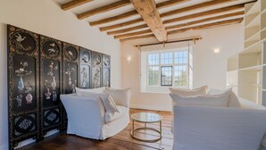 Una habitación con un sofá blanco, una mesita de centro redonda de cristal y un ventanal con vistas a zonas verdes.