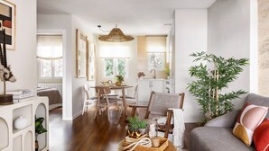 Un soggiorno moderno con un divano grigio, un tavolino da caffè con oggetti decorativi, una zona pranzo con tavolo e sedie e una cucina sullo sfondo.