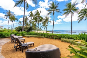 Une terrasse au bord de la plage, dotée de chaises longues et d’un espace repas, le tout entouré de palmiers et offrant une vue sur l’océan.
