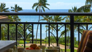 Ein Balkon mit Blick auf das Meer und Palmen, ein Tisch mit Schalen und Früchten sowie ein Stuhl.