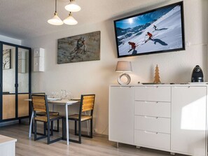Un comedor moderno con un armario blanco, un televisor mostrando una escena de esquí y un cuadro en la pared.