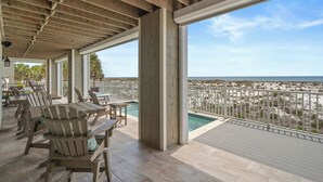 Un espacio exterior cubierto con mobiliario de madera, una piscina y vistas a la playa.