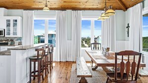 A spacious kitchen with a large island, wooden ceiling, and large windows offering a view of the surrounding area.