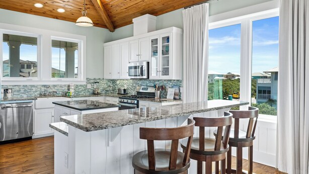 A modern kitchen with white cabinets, a granite countertop, and a large island with bar stools.