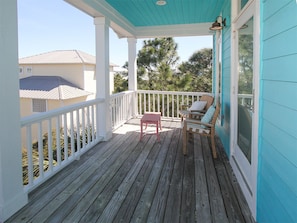 A wooden deck with a white railing, a small pink table, and two wooden chairs with cushions.