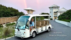 A beach shuttle with a driver, a covered seating area, and a sign indicating it's a free shuttle service. - Tropical Holiday house at Kiva Dunes (Gulf Shores)