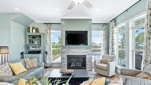 A spacious living room with a fireplace, comfortable seating, and large windows offering a view of the outdoors. - Tropical Holiday house at Kiva Dunes (Gulf Shores)