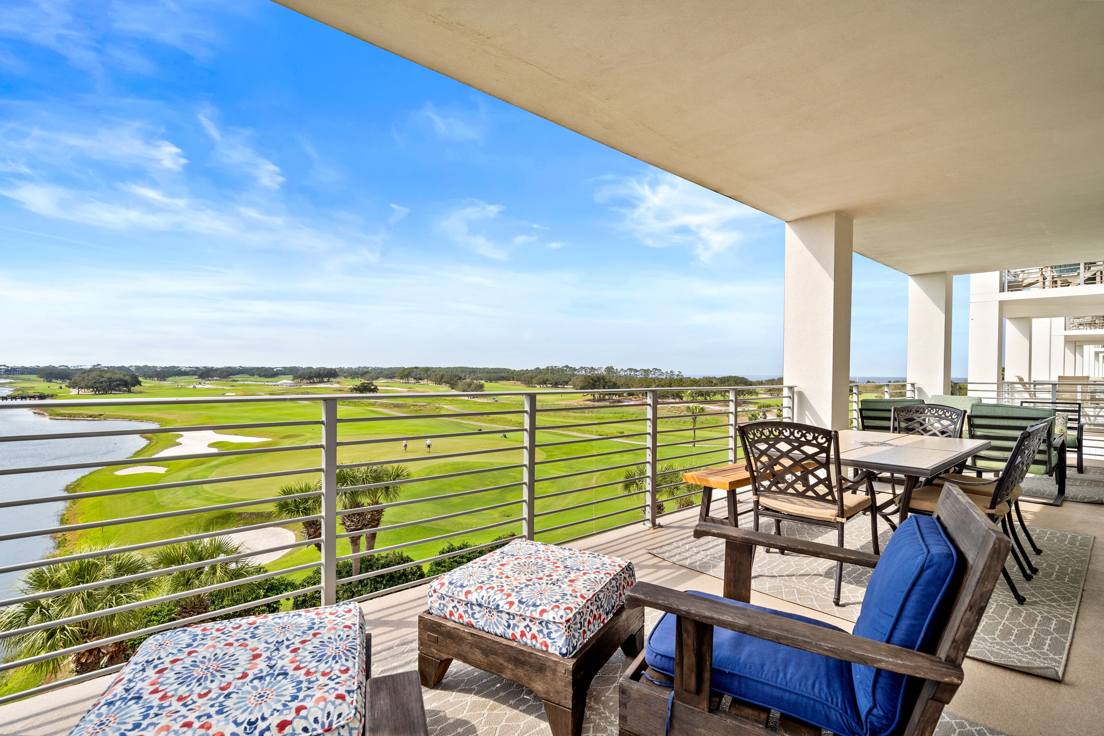 A balcony with outdoor furniture, a view of a golf course, and a body of water.