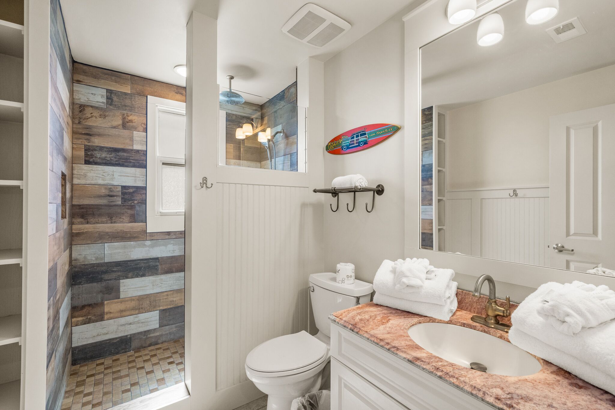 A bathroom with a wooden wall, a shower, a toilet, a sink with a marble countertop, and a large mirror.