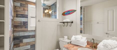A bathroom with a wooden wall, a shower, a toilet, a sink with a marble countertop, and a large mirror.