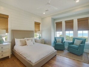 Een slaapkamer met een groot bed, twee nachtkastjes, een plafondventilator en twee stoelen bij een raam met uitzicht.