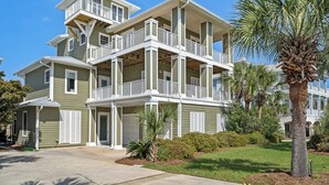 Un immeuble résidentiel à plusieurs étages, doté de balcons, d’un garage et d’une pelouse bien entretenue agrémentée de palmiers.