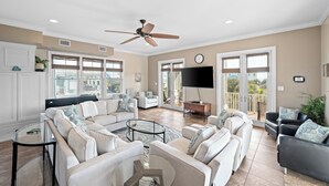 Un salon spacieux doté d’un ventilateur de plafond, de grandes fenêtres, d’un téléviseur à écran plat et d’un balcon.