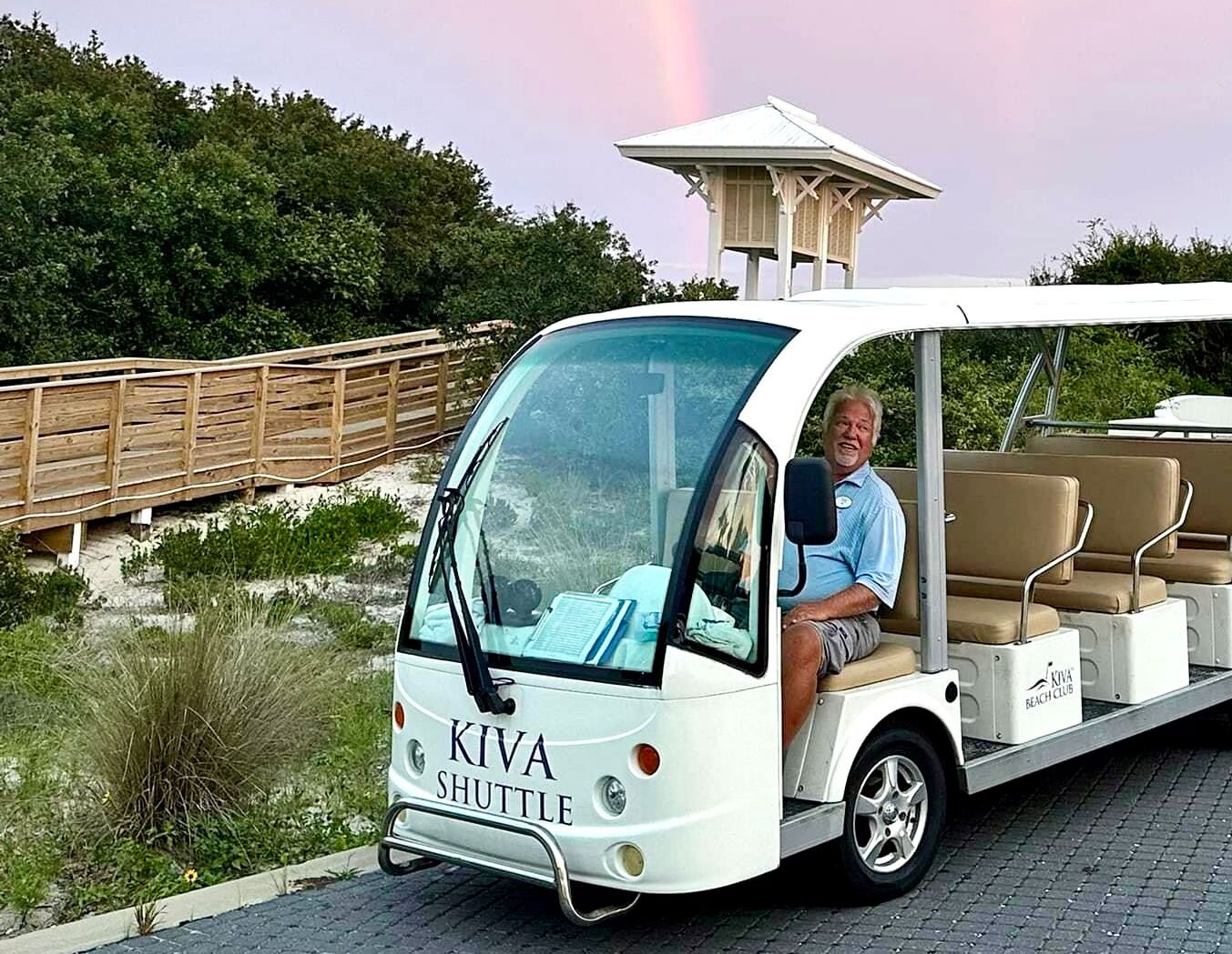 Ein weißer Kiva Shuttle mit Fahrer, ein hölzerner Steg und ein Gazebo im Hintergrund.