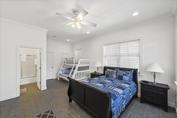 A bedroom with a bed, a nightstand, a lamp, a ceiling fan, a window with blinds, a door, and a staircase leading to a bathroom. - Seabiscuit house at Kiva Dunes (Gulf Shores)