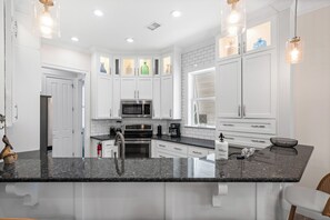 A modern kitchen with white cabinetry, granite countertops, stainless steel appliances, and pendant lighting.