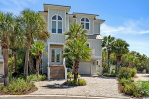 A two-story house with a front entrance, a driveway, and a well-maintained garden with palm trees and shrubs.
