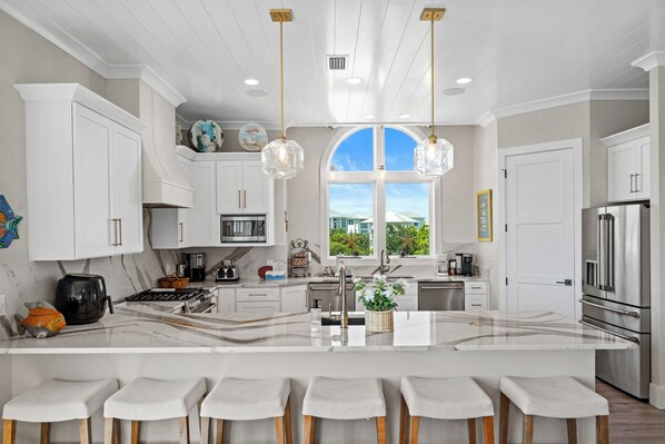 A modern kitchen with a large island, bar stools, and a view of the outdoors through a large window.