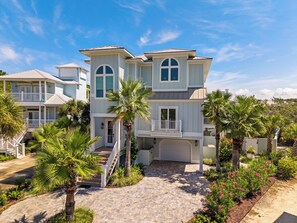 A two-story house with a covered porch, a garage, and a landscaped garden with palm trees and flowering plants.