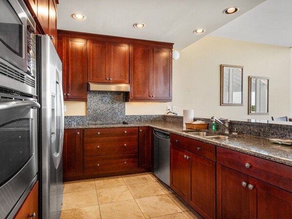 A kitchen with wooden cabinets, stainless steel appliances, granite countertops, and recessed ceiling lights.