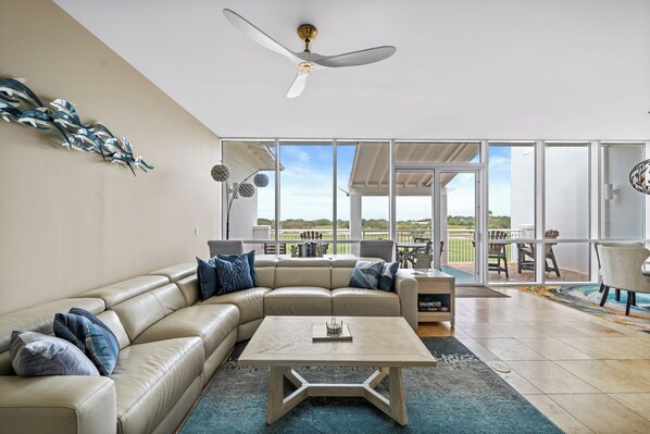 A spacious living room with a large L-shaped beige leather sofa, a coffee table, and a ceiling fan.