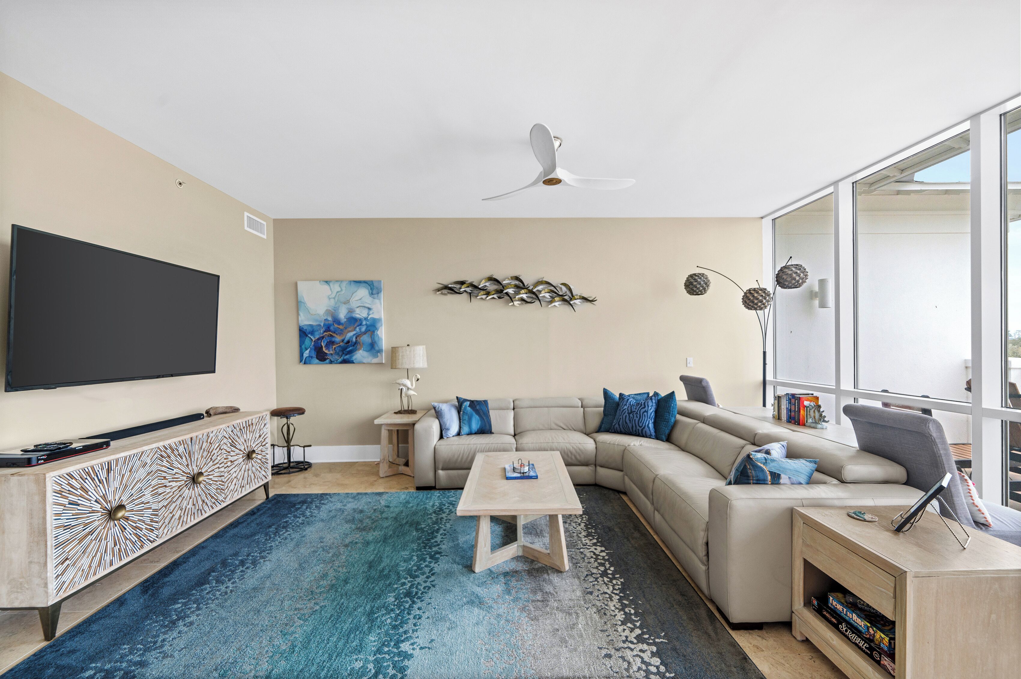 A modern living room with a flat-screen TV, a sectional sofa, a coffee table, and a large window.