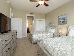 A bedroom with two beds, a dresser, a ceiling fan, and a painting on the wall.